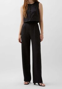 Svart, ärmlös crop top med knäppning framtill och texturmönster, matchad med högmidjade, vida byxor, båda i ett slätt tyg.