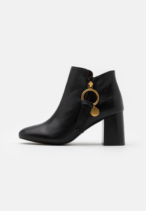 Bottine en cuir noir avec talon bloc et fermeture éclair latérale, ornée d'un anneau doré et d'un petit pendentif rond.