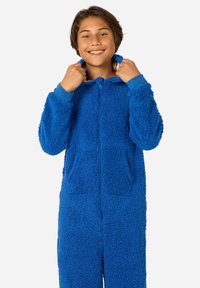 Modra puhasta flisasta enodelna obleka z zadrgo spredaj, ki ima kapuco, elastične manšete in dva sprednja žepa; teksturirana, udobna tkanina.