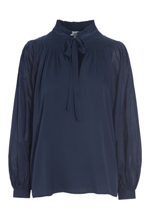 Blusa blu navy con colletto alto, caratterizzata da un davanti legato, dettagli smock e maniche lunghe in tessuto trasparente con polsini arricciati. Texture liscia.