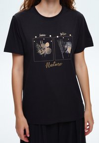 Czarna bawełniana koszulka z złotymi nadrukami roślin i kół oraz napisami "sun" i "rise" nad wzorami, a poniżej "Nature".