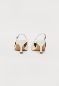 Zapatos de tacón bajo de charol blanco con tira en el tobillo, que cuentan con una correa delgada y un acabado suave y brillante.