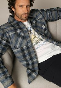 Gestreepte ritsjack in blauw, grijs en wit met een gestructureerde stof. Heeft een borstzak en een logotag aan de linkerkant.