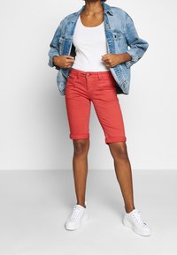 Punaiset denimhousut, joihin on käännetty lahkeet, yhdistettynä valkoiseen topiin ja vaalean pestyyn denimtakkiin, täydentää valkoiset tennarit.