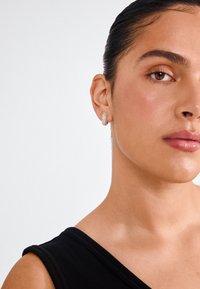 Boucles d'oreilles créoles dorées ornées de strass transparents, avec une surface texturée et une finition polie, portées par un modèle.