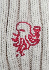 Suéter de punto crema con un patrón de canalé texturizado y un diseño de pulpo bordado en rojo en el centro, enfatizando los detalles y la artesanía.