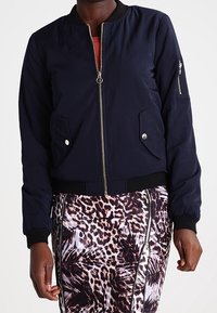 Navy bomberjacka med dragkedja, ribbade manschetter och sidofickor. Slät textur, lätt material och en minimalistisk design.