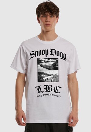 Nuori mies pukeutuneena valkoiseen T-paitaan, jossa mustaa tekstiä "Snoop Dogg", "LBC" ja mustavalkoisia kuvia vintage-autoista.