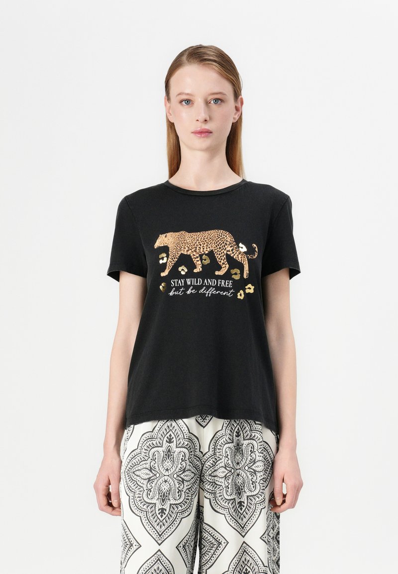 T-shirt en coton noir avec un graphique de léopard doré et le texte "RESTEZ SAUVAGE ET LIBRE mais soyez différent" en blanc, avec des manches courtes et un col rond.