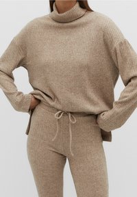 Beżowy sweter z golfem, prążkowany, z długimi rękawami i luźnym krojem, zestawiony z dopasowanymi spodniami z wysokim stanem, prążkowanymi, z troczkami.