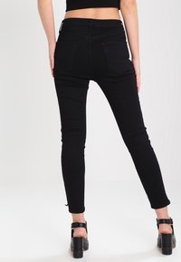 Černé skinny džíny s vysokým pasem, hladkou strukturou, zadními kapsami a přizpůsobeným střihem, doplněné černými vysokými podpatky.