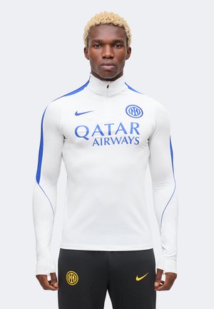 Modello maschile con capelli biondi corti che indossa un top sportivo bianco a manica lunga con zip con loghi blu di Qatar Airways e Inter Milan.