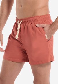 Punaiset uimalahkeet, jotka on valmistettu kevyestä materiaalista. Niissä on joustava vyötärö, jossa on naru ja sivutaskut.