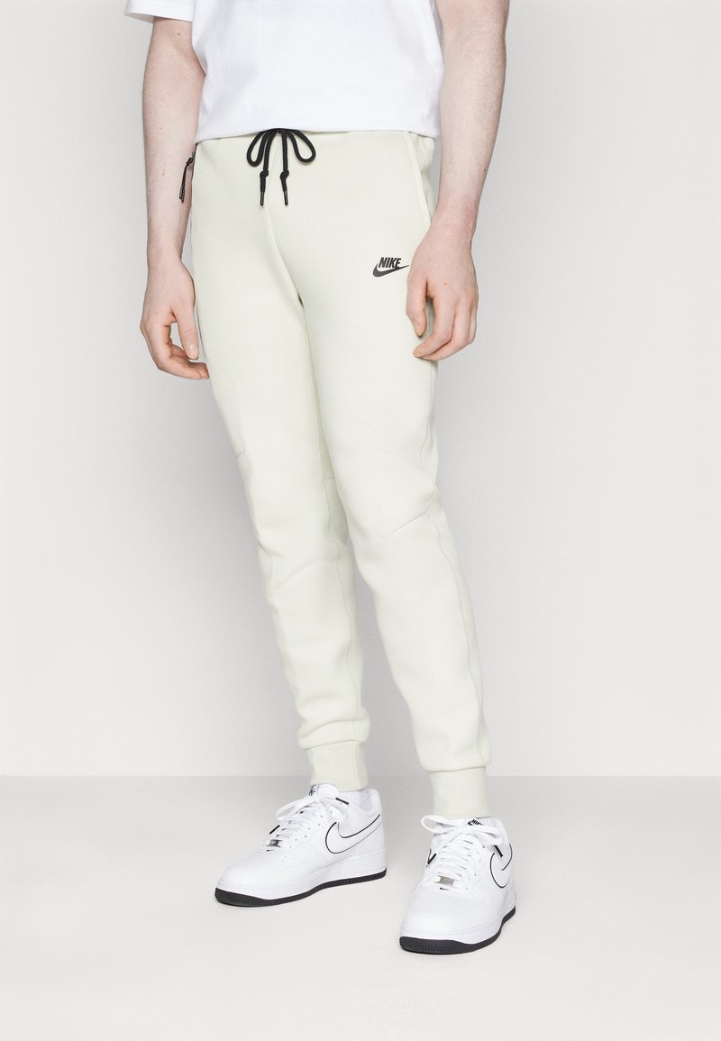 Hellbeige Nike-Sweatpants mit schwarzem Kordelzug, taillierter Passform, seitlichen Taschen und schwarzem Logo. Kombiniert mit weißen Nike-Sneakern.