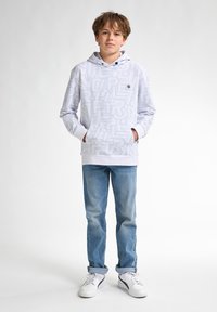 Witte hoodie met lichtblauwe tekstpatronen, voorzak en trekkoordkap, gecombineerd met lichtblauwe jeans en witte sneakers.