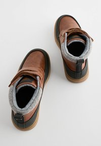 Bottines en cuir marron avec doublure en polaire grise, sangle Velcro, semelle en caoutchouc noir et finition texturée. Design à bout arrondi.