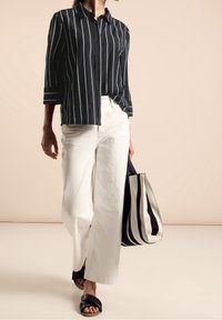 Chemise à rayures noires et blanches, pantalon large blanc, et sac fourre-tout à rayures noir et blanc, associés à des sandales plates noires.