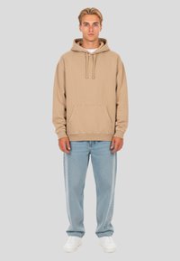 Felpa beige in morbido tessuto con tasca frontale, stringhe al collo, abbinata a jeans azzurri chiari e sneakers bianche.