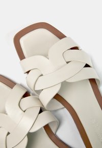 Sandales en cuir blanc avec des lanières tressées, une forme de bout carré et une semelle brune contrastante. Texture lisse avec peu de matériel.