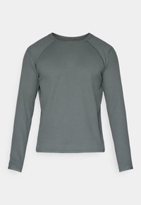 T-shirt à manches longues de couleur vert foncé, fabriqué en matériau texturé et côtelé, avec un col rond et des manches raglan.