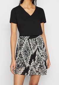 Top negro de manga corta con escote en V, combinado con una falda de estampado que presenta diseños geométricos en negro, blanco y gris; textura plisada.