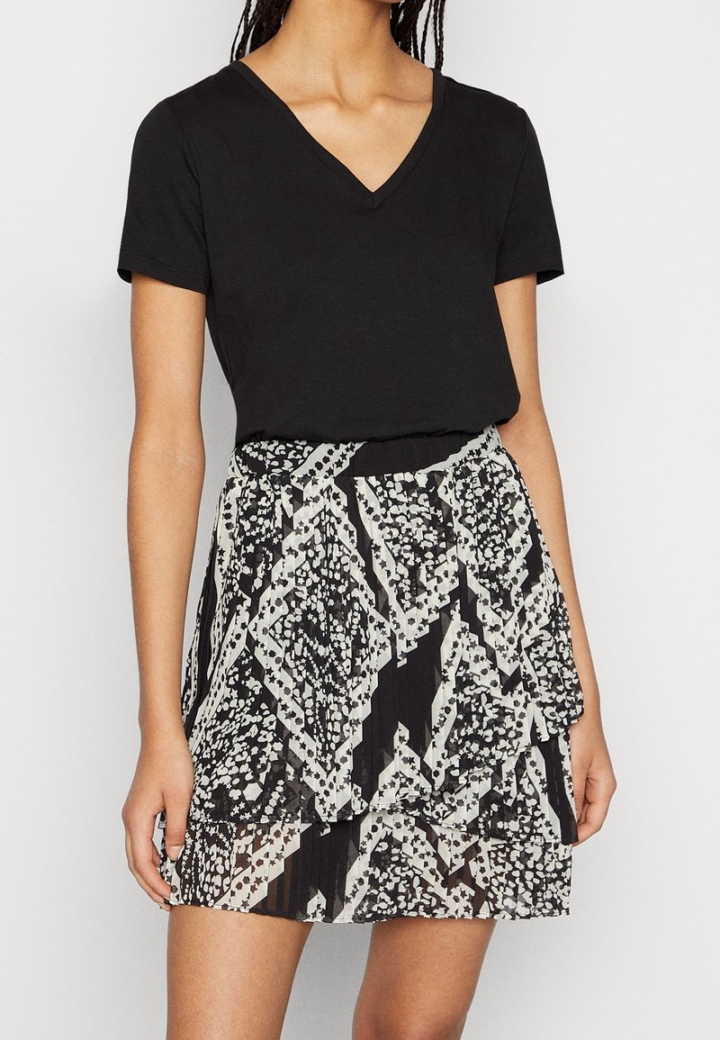Top negro de manga corta con escote en V, combinado con una falda de estampado que presenta diseños geométricos en negro, blanco y gris; textura plisada.