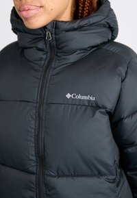 Černá péřová bunda s vysokým límcem, na zip, s prošívanými sekcemi a logem Columbia na levém prsou.