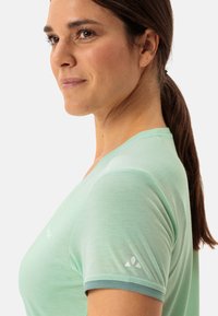 Light green athletic T-shirt with a V-neck, short sleeves, and a logo detail on the left sleeve. Soft, breathable fabric.