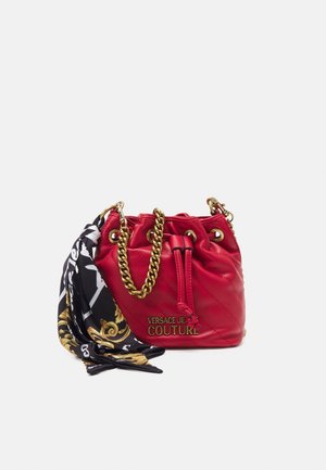 Rød quiltet læder bucket taske med guldkæde som håndtag og snøre-lukning, pyntet med et sort og guld mønstret tørklæde.