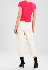 En figursydd rosa kortärmad topp i kombination med krämfärgade tapered byxor; modellen bär svarta högklackade strumpor som visar upp en avslappnad stil.