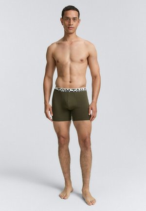 Olivengrüne Boxershorts für Herren mit einem schwarz-weißen, gebrandeten Bündchen, aus weichem Material, mit einer figurbetonten Passform.