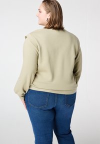 Lichtgroene trui met een ontspannen pasvorm, met een uniek schouderontwerp en gedetailleerde manchetten, gecombineerd met donkerblauwe jeans.