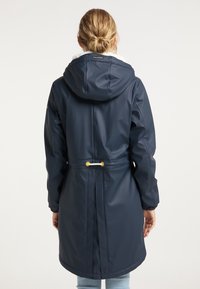 Laivastonsininen vedenpitävä takki, jossa on huppu, kiristettävä vyötärö ja pehmeä tekoturkisvuori kauluksessa. Varustettu kultaisilla yksityiskohdilla ja joustavilla hihansuilla.