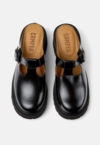 Pantofi din piele neagră cu un design tip T-strap, cataramă ajustabilă și branț căptușit de culoare bej, având o talpă din cauciuc negru, groasă.