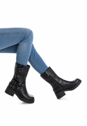 Stivaletti neri in pelle con tacchi chunky, caratterizzati da dettagli in fibbia e cinturino. Texture liscia e una zip laterale.