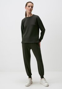 Donkergroene sweatshirt en jogger set van zachte stof. Kenmerkt zich door een relaxte pasvorm, lange mouwen en taps toelopende broeken met elastische boorden.