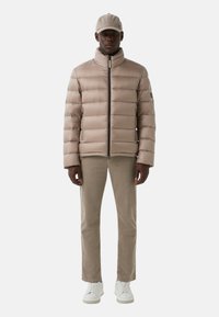 Pufjakke i lys beige med højt krave og lynlås, parret med beige kordfløjl bukser og hvide sneakers.