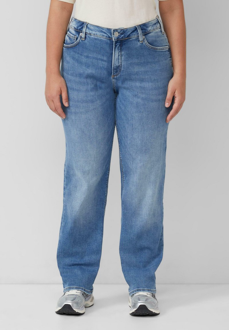 Jean en denim bleu délavé avec une coupe droite, poches avant et fermeture à bouton. Assortis avec des chaussures de sport grises.