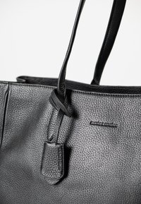 Zwarte leren tote bag met een gestructureerd oppervlak, voorzien van twee lange handvatten en een klein leren label met het merknamen in reliëf.