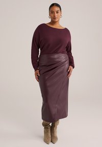 Bordeauxfarbene Strickoberteil mit weitem Ausschnitt, kombiniert mit einem hoch taillierten, strukturierten Leder-Midi-Rock mit Drapé-Design. Wildleder-Ankle-Boots.