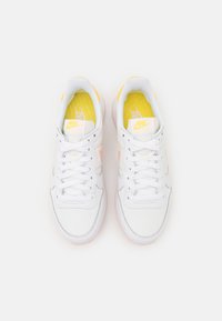 Pair of white Nike sneakers with yellow insoles and pink accents, viewed from above on a white background.