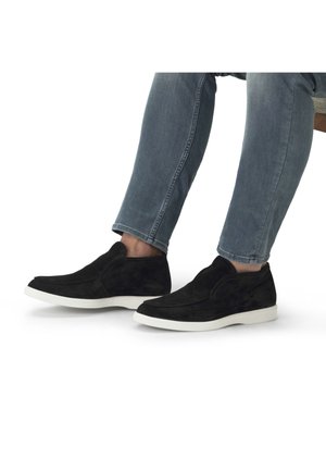 Schwarze Wildleder Slipper mit einer weißen Gummisohle, die ein elegantes Design und nahtlose Konstruktion aufweisen, kombiniert mit blauen Denim-Jeans.