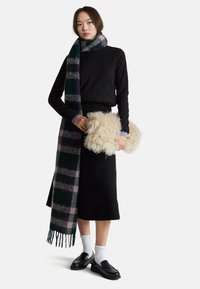 Maglione nero a coste, gonna lunga nera, sciarpa scozzese verde e viola, borsa a tracolla beige pelosa, calzini bianchi, mocassini neri.