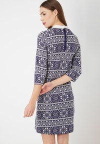 Mujer de espaldas que lleva un vestido con estampado en azul marino y blanco, con mangas 3/4, un cuello blanco y detalles de botones en la parte de atrás.