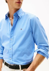 Blauw geruit overhemd met knopen en een klassieke kraag, voorzien van witte knopen en een klein logo op de borst. Een zwarte geweven riem maakt de look compleet.