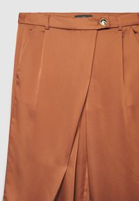 Pantalon en satin marron à la texture lisse, avec un pli à l'avant et une fermeture par bouton doré à la taille.