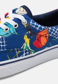 Blå canvas sneakers med vita snören, prydda med färgglada tryck av solglasögon, en röd keps och en gul polo-spelare logotyp.