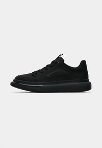 Baskets noires avec une texture lisse, dotées d'une semelle épaisse, d'un design à lacets et de détails de logo sur le côté. Esthétique minimaliste.