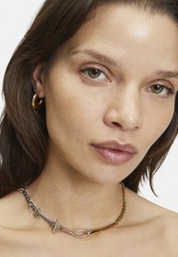 Gold- und Silberschmuckkette mit einem Hakenverschluss, die glatte und strukturierte Glieder aufweist. Nahaufnahme, die die filigranen Details zeigt.