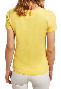 Żółta bawełniana koszulka z okrągłym dekoltem i krótkimi rękawami, o gładkiej teksturze i dopasowanym kroju, pokazana od tyłu.
